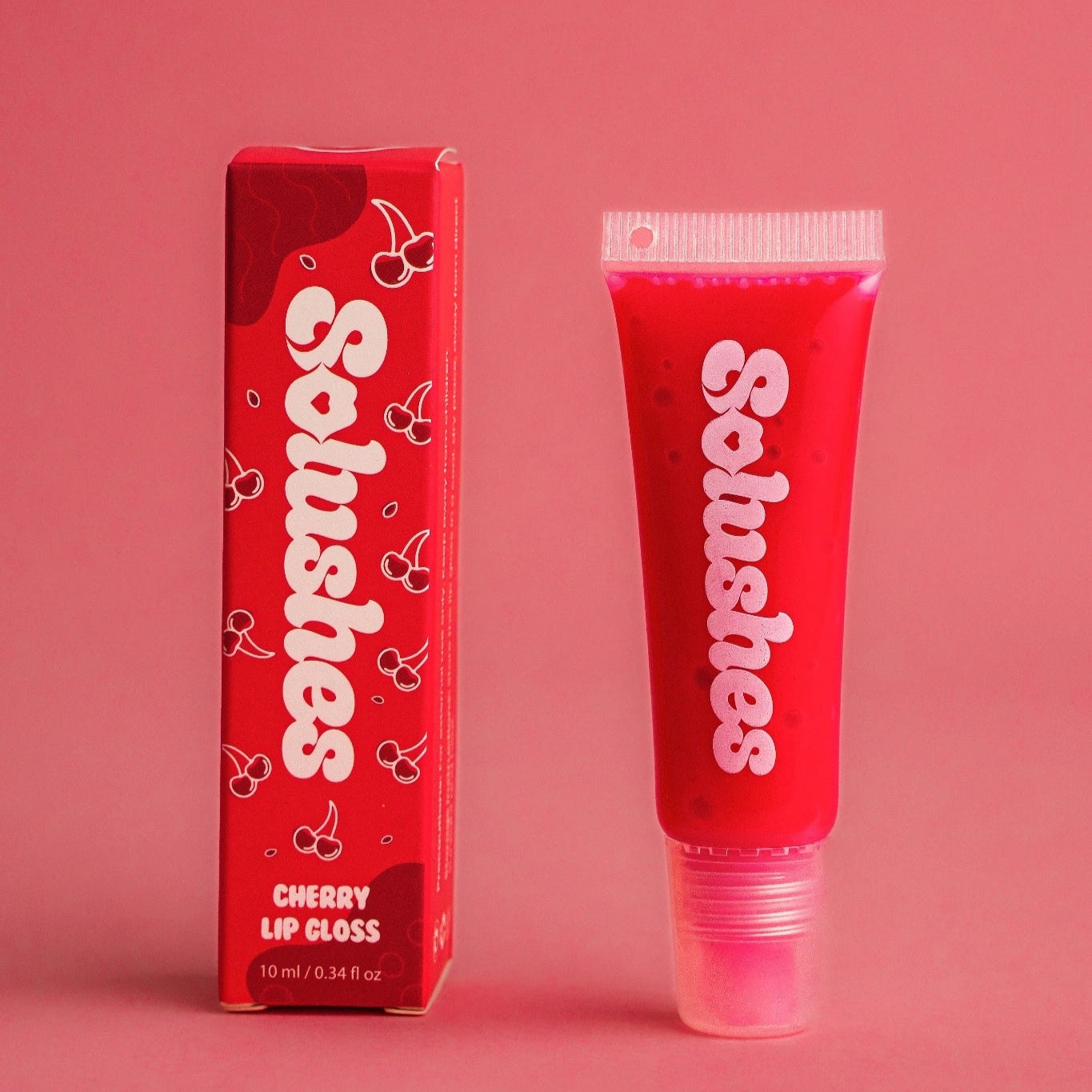 Cherry lip gloss tube and packaging with 'Solushes' branding on a pink background