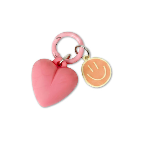 Pink heart-shaped keychain with a smiley face charm on a white background